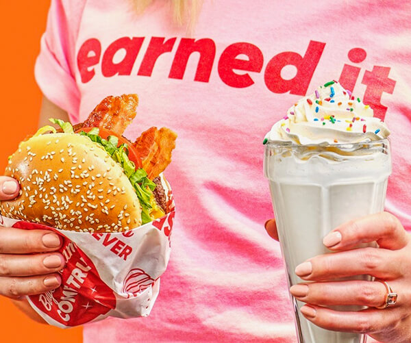 Person wearing "earned it" t-shirt holding a Bacon Cheeseburger and Chocolate Shake
